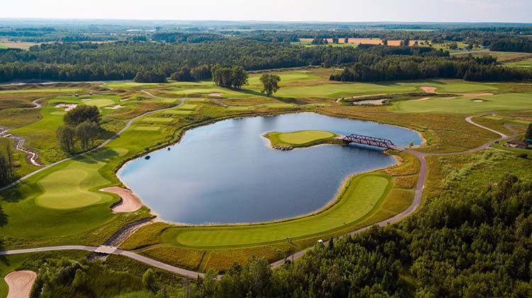 #15 at Sweetgrass Golf Club An aerial view of hole number 15 at Sweetgrass Golf Club. An isand green is surrounded by water within a small lake.