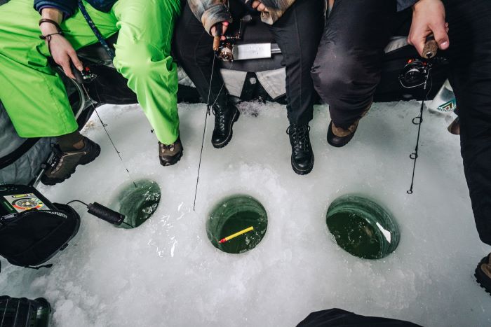 A group of fishes sitting around holes in ice, waiting for fish to bite.